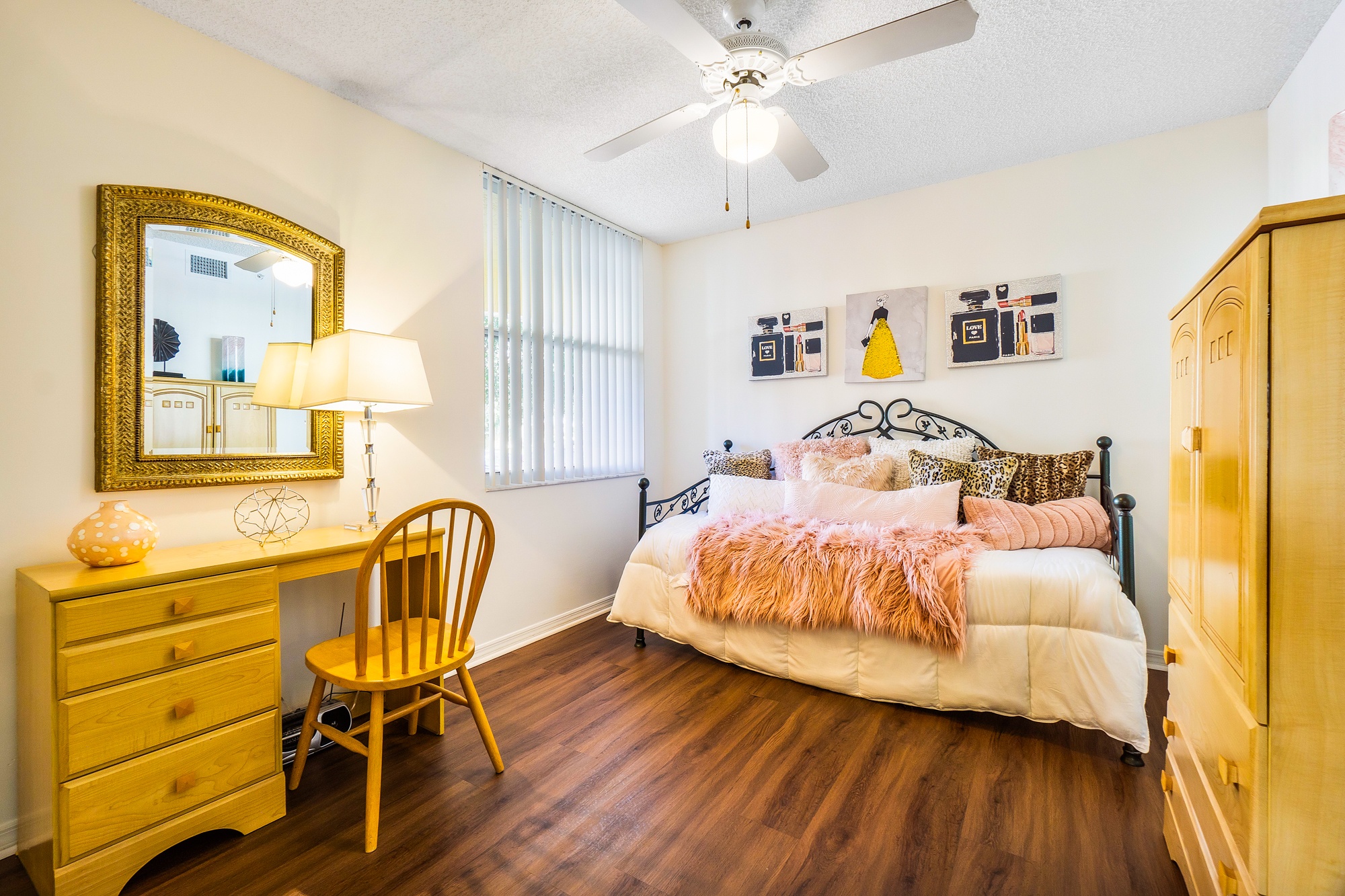 A bedroom with a bed, a desk, a chair, and a ceiling fan.